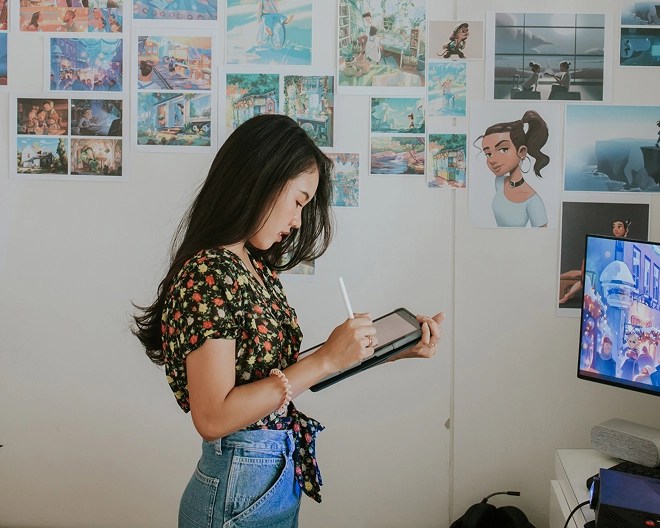 Person using a tablet and stylus in a creative workspace decorated with vibrant illustrations, plants, and digital screens.