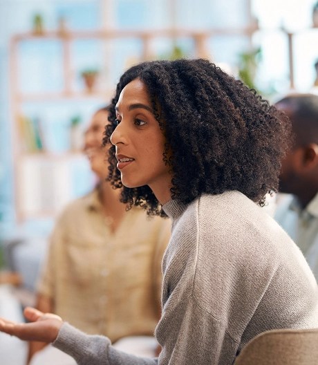 Profile of a woman in a white sweater speaking to a group therapy session, engaging the participants in discussion.