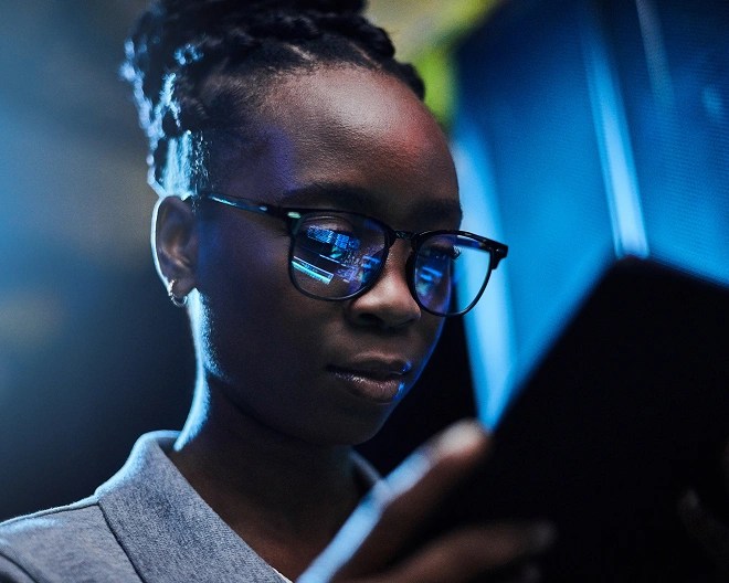 Person in a collared shirt and glasses looking at a tablet, with code reflected in their lenses.