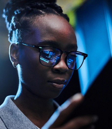 Person in a collared shirt and glasses looking at a tablet, with code reflected in their lenses.