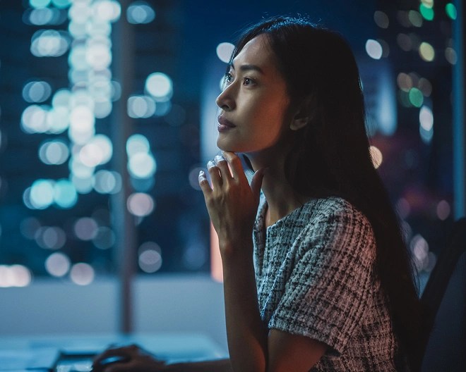 Person sitting at a desk and gazing out a window at a glowing cityscape