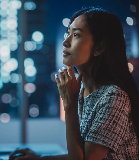 Person sitting at a desk and gazing out a window at a glowing cityscape