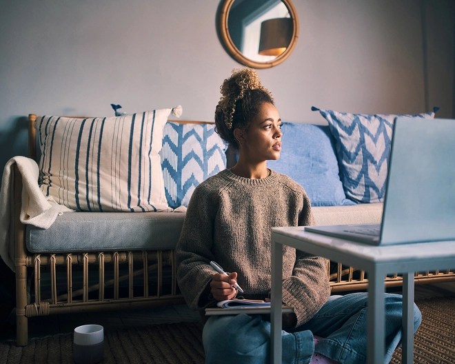 Person sitting on the floor with a notebook and laptop at a low table in a relaxed living space.