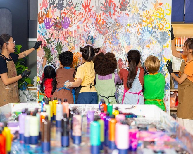 Children and an adult creating a handprint mural together in a colourful art classroom.