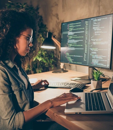Individual working at a desk with a laptop and external monitor displaying lines of code.
