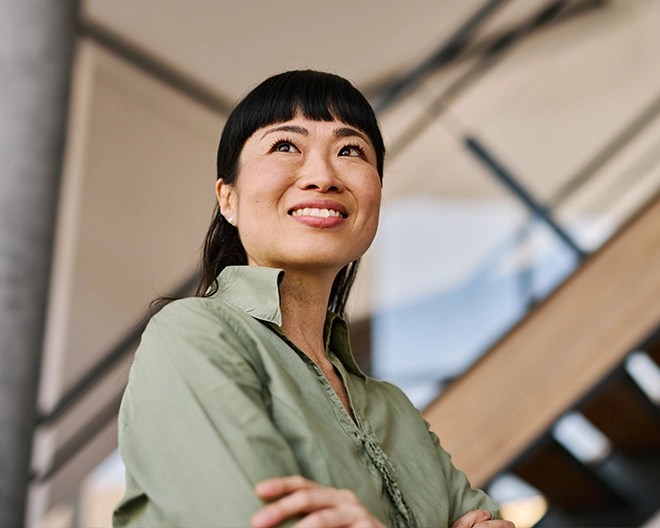Individual in a light green button-up shirt standing indoors near a staircase with wooden steps and metal railings, looking slightly upward with a pleasant expression.