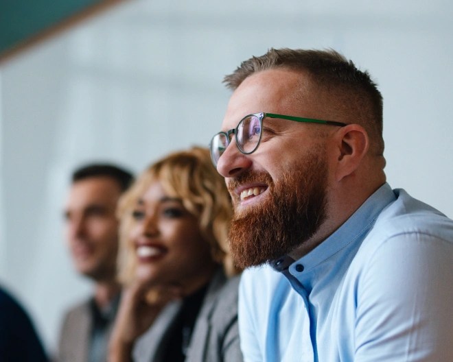 A man wearing a light blue shirt smiling with smartly-dressed colleagues.