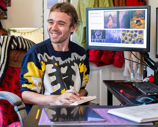 Student with notepad smiling in front of computer and monitor