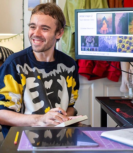 Student with notepad smiling in front of computer and monitor