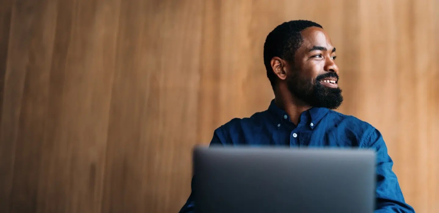 A professional, seated in front of an open laptop, wearing a dark blue shirt, smiling and looking to the side.