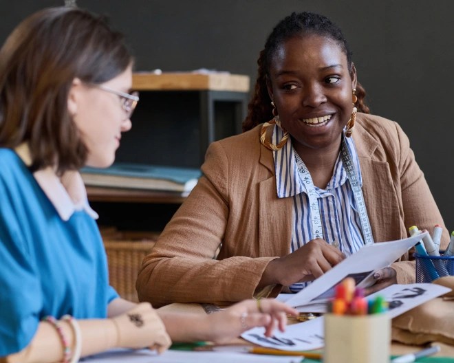 two women sat in a classroom smiling and talking