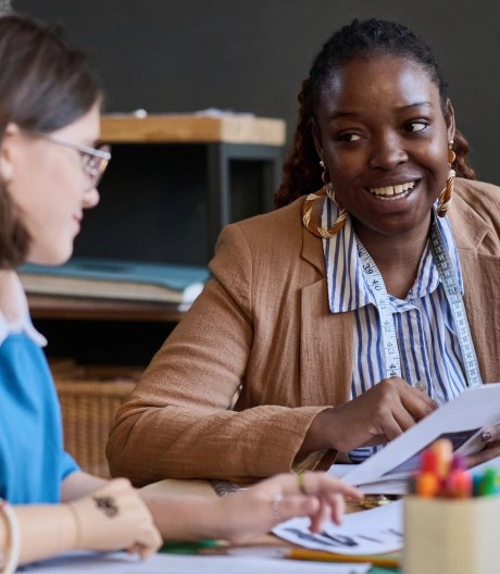 two women sat in a classroom smiling and talking